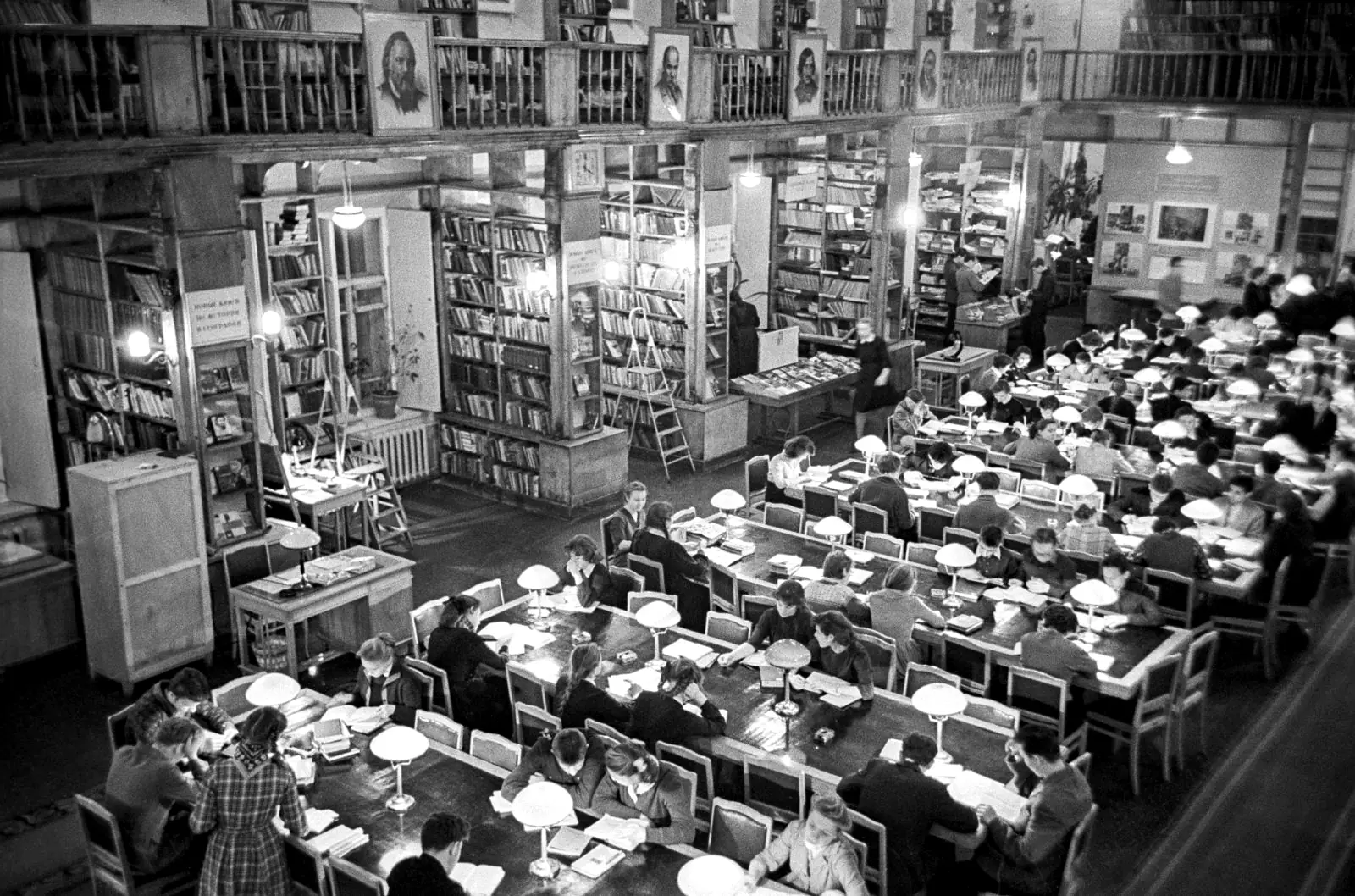 The reading room of the Russian State Library, Moscow, in 1962: long desks with reading lamps, full of people, shelves to the ceiling.